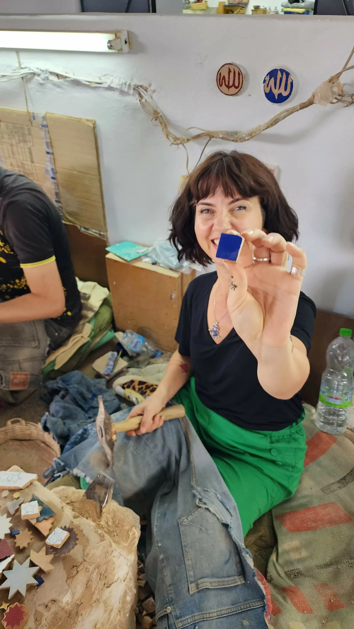 Participante cortando peças de zellige à mão, em uma oficina de mosaico