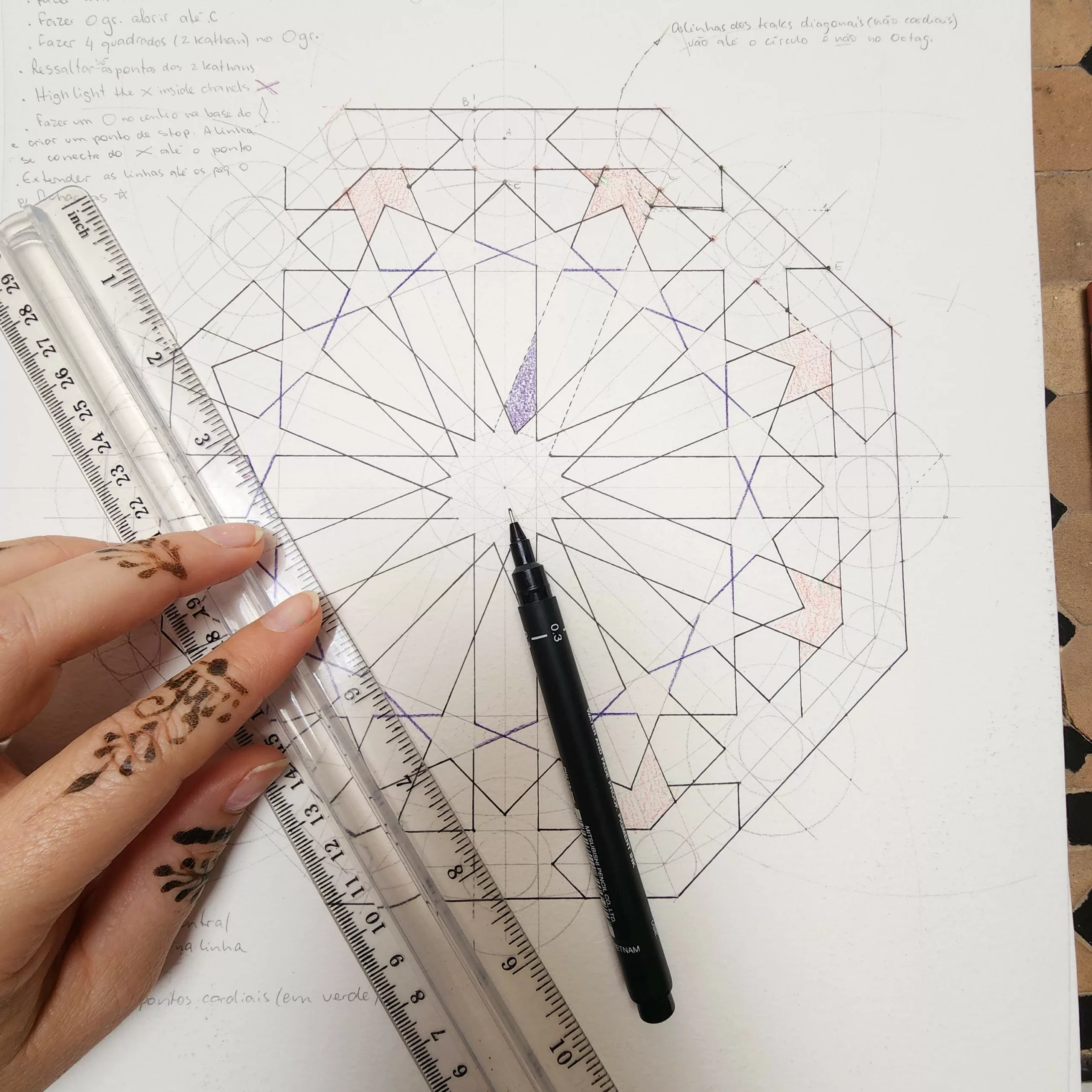 Mão pintada com henna desenhando a construção de uma estrela de oito pontas, com régua e nanquim