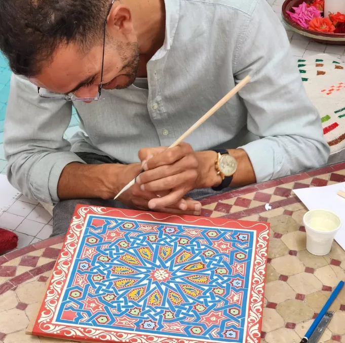 Artista marroquino pintando um padrão tradicional de zouak em madeira