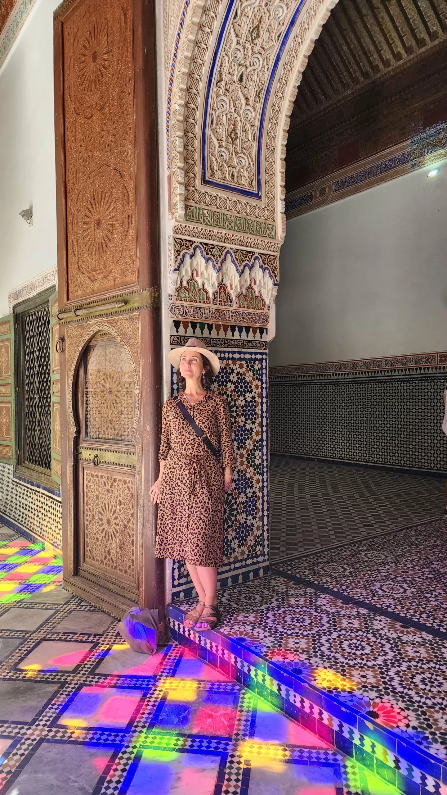 Mulher junto a um arco ornamentado, com luz colorida de vitral refletida no chão de zellige